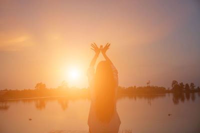 Silhouette person standing by lake against sky during sunset