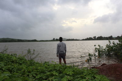 Rear view of man standing by lake against sky
