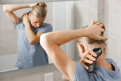 Personal hygiene, caucasian man cutting his own hair in the bathroom with wireless electric shaver