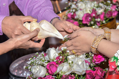 Cropped image of man and woman holding seashell over bride hands during wedding ceremony