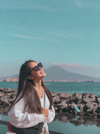 Young woman wearing sunglasses standing by sea against sky