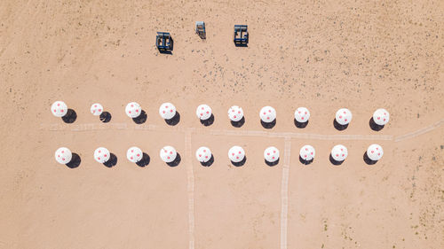 An empty clean sandy beach with two rows of parasols and cabanas, aerial view. 