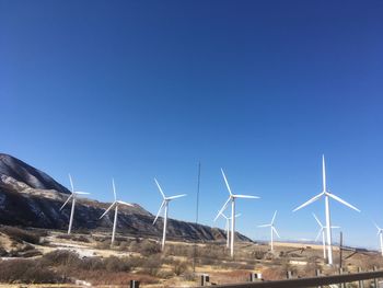 Windmills on landscape against clear blue sky