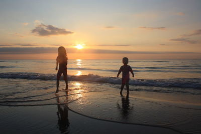 Full length of silhouette playful siblings on shore during sunset