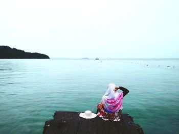 Rear view of woman sitting by sea against clear sky