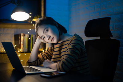 Portrait of woman sitting by laptop at home