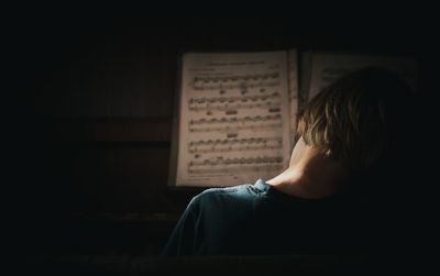 Rear view of boy playing piano while playing piano with music note at home