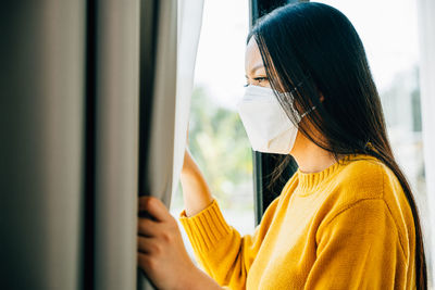 Side view of young woman looking through window