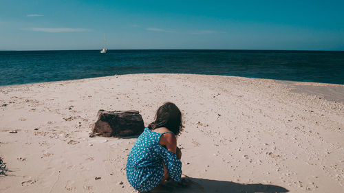 Rear view of woman sitting on beach against sea