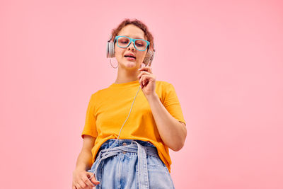 Portrait of young woman wearing sunglasses while standing against pink background