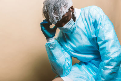 Doctor wearing mask sitting against colored background