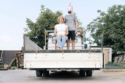 Man wearing horse mask standing by woman in truck