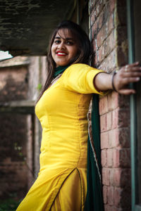 Portrait of smiling young woman standing by wall