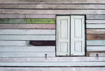 Old grunged wooden window frame painted white vintage with old colourful plywood wall. 