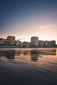 Buildings by sea against sky during sunset in city