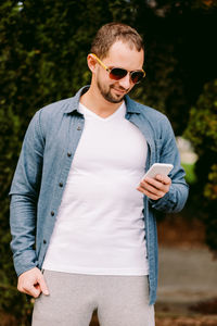 Portrait of young man wearing sunglasses standing against trees