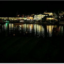 Illuminated city by river against sky at night