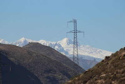 Electricity pylons on mountain against clear sky