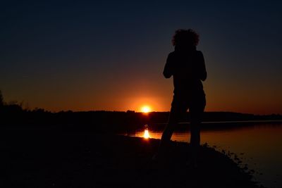 Silhouette man standing on shore against sky during sunset