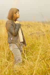 Young woman standing on grassy field against sky