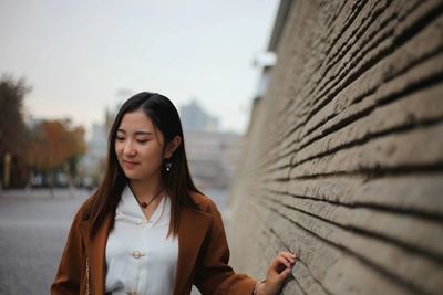 Smiling young woman standing by wall in city