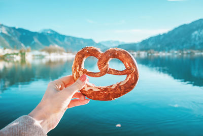 Hand with traditional bread on the mountain lake background in bavarian alps, germany.