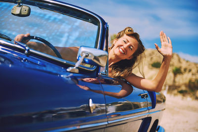 Smiling woman waving hand while driving car