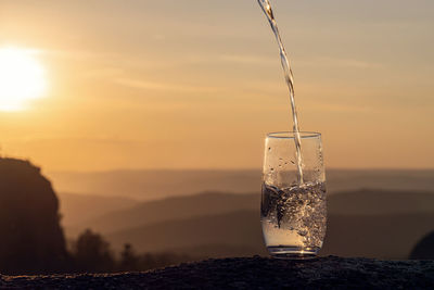 Close-up of glass of water against sky during sunset