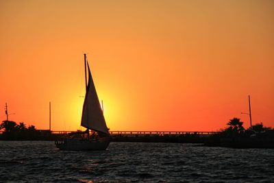 Silhouette sailboat sailing on sea against orange sky