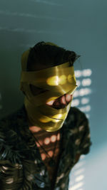 Close-up of man with yellow adhesive tape rolled on face against wall