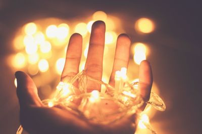 Cropped hand of person holding illuminated string lights at home