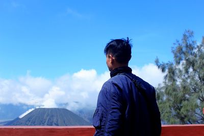 Rear view of man standing against blue sky