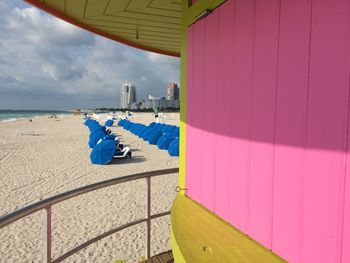 Umbrellas seen from lifeguard hut at beach against cloudy sky