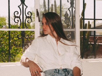 Woman standing by window against fence