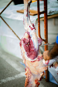 A man with a knife is cuttting the meat hanging on the hook.