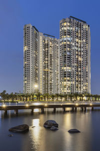 Illuminated buildings by river against sky at dusk