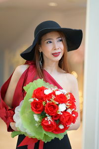 Portrait of smiling woman standing against red rose