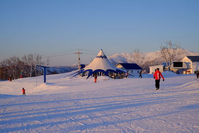 People on snow covered field against clear sky