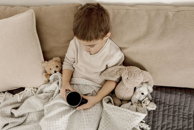 Sick little boy drinking hot tea on the bed at home. unwell, illness child wrapped in a blanket, 