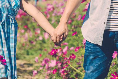 Midsection of couple holding hands while walking by flowering plants