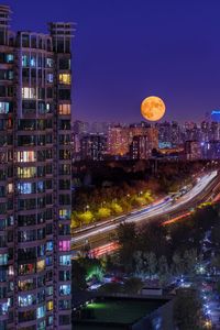 Full moon over cityscape at night with an apartment building in the foreground