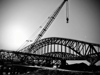 Low angle view of crane by arch bridge against sky