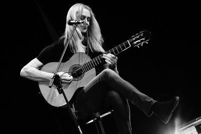 Man playing guitar against black background