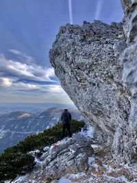 Man standing on rock by mountain against sky