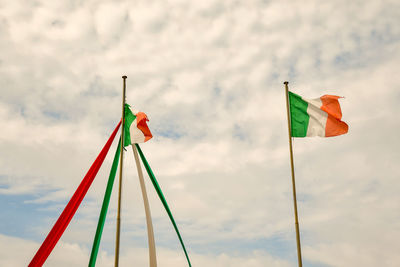 Two italian national flags flying against blue cloudy sky 