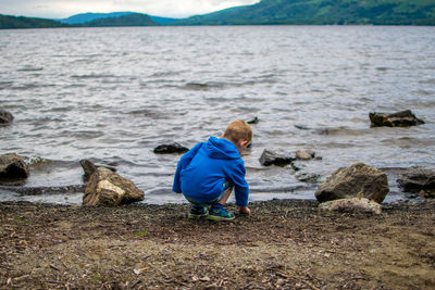 Rear view of boy crouching at riverbank