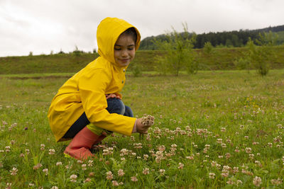 Child in nature under sun with a yellow rain coat