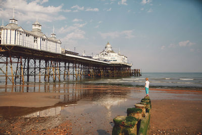 Person viewing built structure on pier against sky