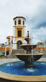 Fountain by building against sky