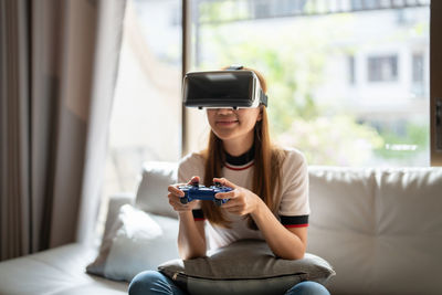 Playful girl with virtual reality headset sitting at home